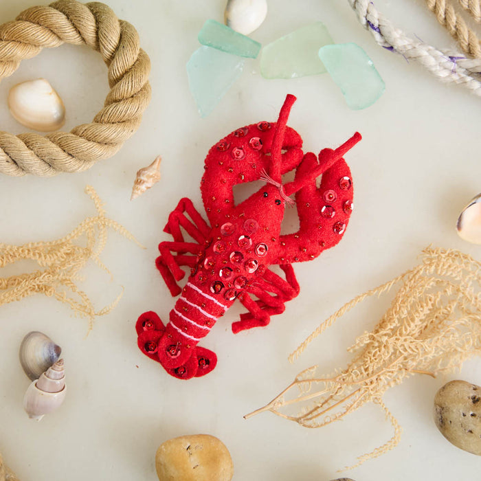 Commemorate the bounty of the northeastern seaboard with our handcrafted Bejeweled Red Lobster Ornament, designed to bring the spirit of coastal Maine to your home. Crafted from vibrant red felt and embellished with sparkling beads and sequins, this festive lobster ornament catches the light beautifully, adding texture, shimmer, and whimsical seaside charm to your holiday décor.