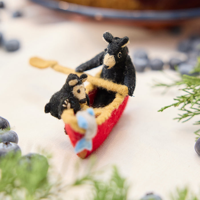 Craftspring’s handmade felt Bears in a Canoe ornament — a mama bear paddling a canoe with a cub climbing over the side, displayed with evergreens and blueberries for a whimsical holiday scene, perfect for Christmas decorating or gifting, ethically crafted by artisans using sustainable wool.