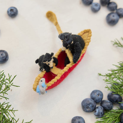 Craftspring’s handmade felt Bears in a Canoe ornament — a mama bear paddling a canoe with a cub climbing over the side, displayed with evergreens and blueberries for a whimsical holiday scene, perfect for Christmas decorating or gifting, ethically crafted by artisans using sustainable wool.