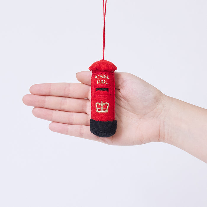 Craftspring’s British Post Box ornament held in front of a hand to show its size—handmade from sustainable wool with a classic red design and gold embroidered details, ethically crafted by artisans using sustainable wool.
