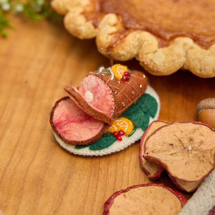 Craftspring’s handmade felt Spiral Ham Platter ornament — a festive ham with intricate beaded and embroidered details, displayed on a harvest table with pumpkin pie for a cozy holiday scene, perfect for Thanksgiving decorating or gifting, ethically crafted by artisans using sustainable wool.