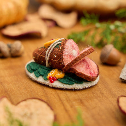 Craftspring’s handmade felt Spiral Ham Platter ornament — a festive ham with intricate beaded and embroidered details, displayed on a harvest table with dried apple slices and pumpkins for a warm holiday scene, perfect for Thanksgiving decorating or gifting, ethically crafted by artisans using sustainable wool.