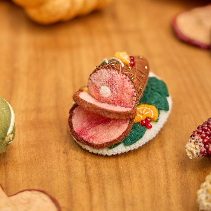 Craftspring’s handmade felt Spiral Ham Platter ornament — a festive ham with intricate beaded and embroidered details, displayed on a harvest table with dried apple slices and pumpkins for a warm holiday scene, perfect for Thanksgiving decorating or gifting, ethically crafted by artisans using sustainable wool.