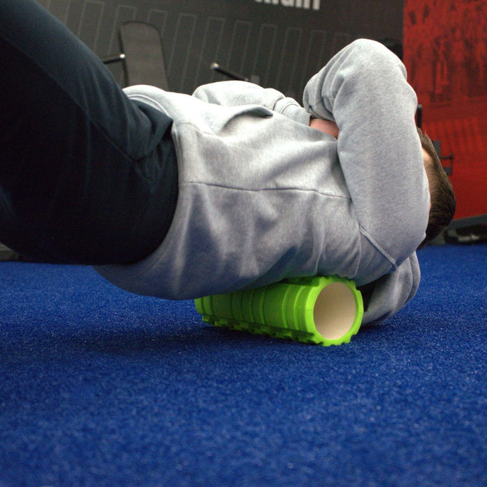 Gronk Fitness green foam roller under back on blue carpet