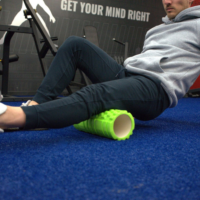 Gronk Fitness green foam roller under thighs on blue carpet