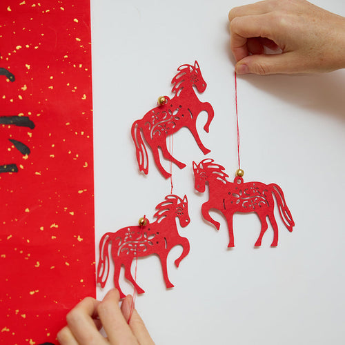 Craftspring’s Paper Horse Ornaments - Set of 3—hands hanging the ornament on a door, showcasing festive Lunar New Year decor and heirloom-quality gifting, ethically handmade by artisans.