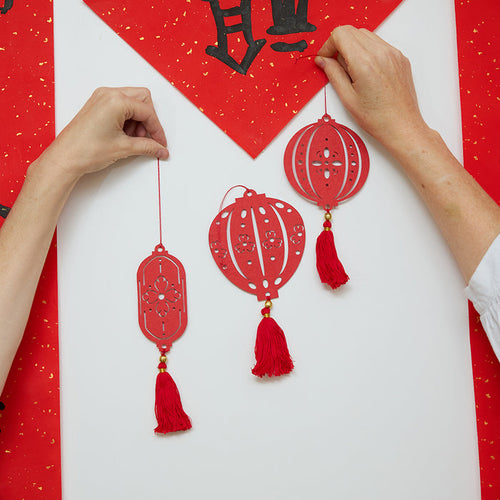 Paper Lantern Ornaments hung on a door with helping hands, showcasing their intricate paper cutout details. Ethically handmade by artisans for joyful Lunar New Year gifting and heirloom decor.