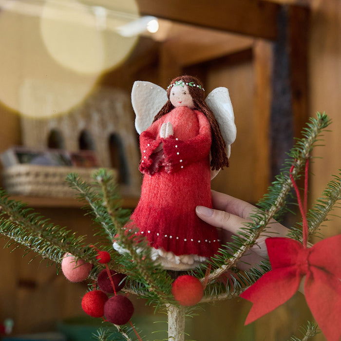 Craftspring’s Praying Angel Tree Topper - Light — felt angel wearing a red dress with white beads, embroidered and beaded wreath crown, and hands in prayer — displayed on top of a Christmas tree, evoking festive warmth, sweet holiday charm, and heirloom-quality Christmas gifting, ethically crafted by artisans using sustainable wool.