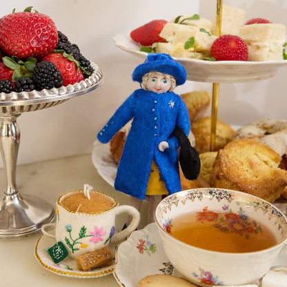 Queen Elizabeth II felt ornament wearing royal blue coat and hat, with black handbag and detailed embroidery. Handmade wool Christmas ornament honoring British royalty. Fair trade and ready to hang. Pictured with afternoon tea foods and a felt tea cup