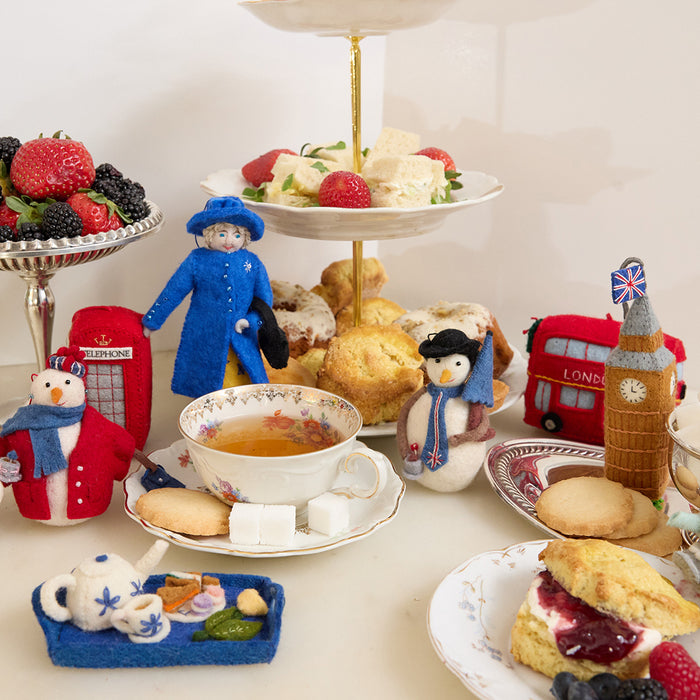 Queen Elizabeth II felt ornament wearing royal blue coat and hat, with black handbag and detailed embroidery. Handmade wool Christmas ornament honoring British royalty. Fair trade and ready to hang. Surrounded by ornaments of iconic British places and foods