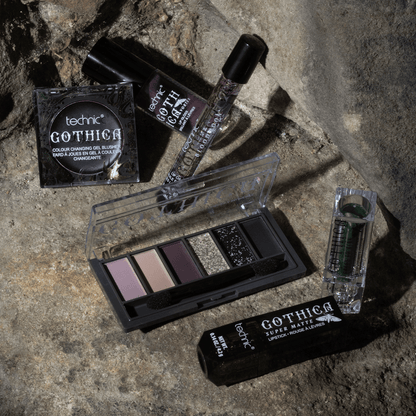 Some other gothica products including lip oils, lipsticks, blusher and eyeshadow palette. This is all on a stone wall background.