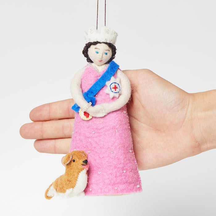 Young Queen Elizabeth II felt ornament in gala attire with a loyal corgi at her side. Handmade wool Christmas ornament honoring British royalty. Fair trade and ready to hang. With hand to show size