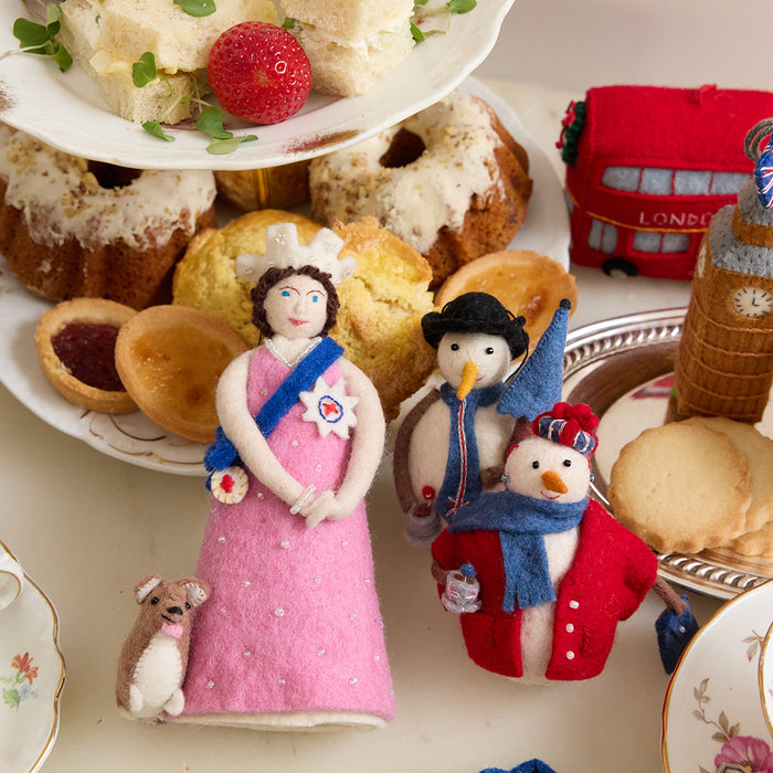 A British ornament collection featuring Young Queen Elizabeth II felt ornament in gala attire with a loyal corgi at her side. Handmade wool Christmas ornament honoring British royalty. Fair trade and ready to hang.